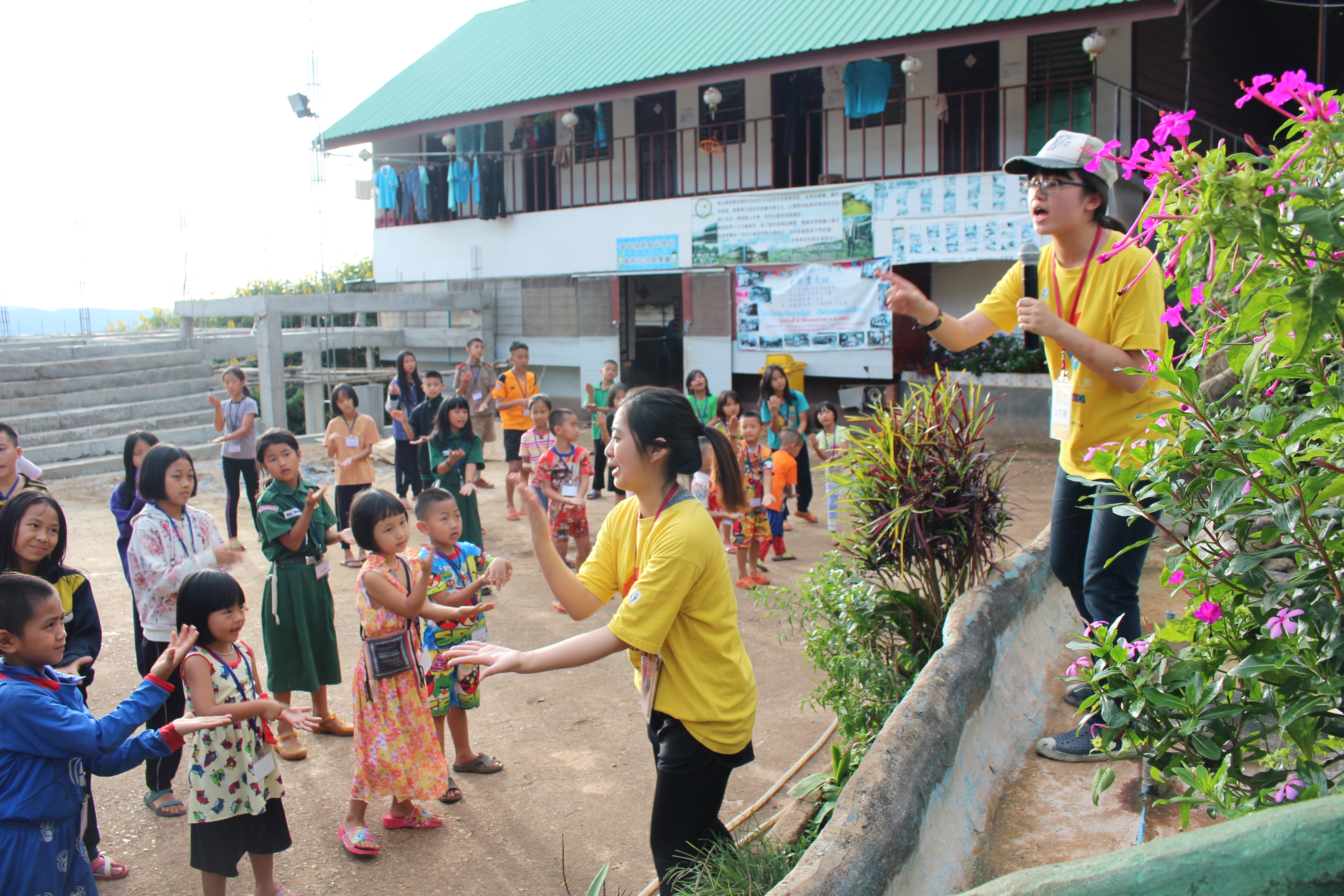 中華非營利組織發展協會「真愛中華志工服務隊」團隊成員江可晴(右1持麥克風者)於泰國清萊府象苗國小帶領小朋友進行肢體律動。